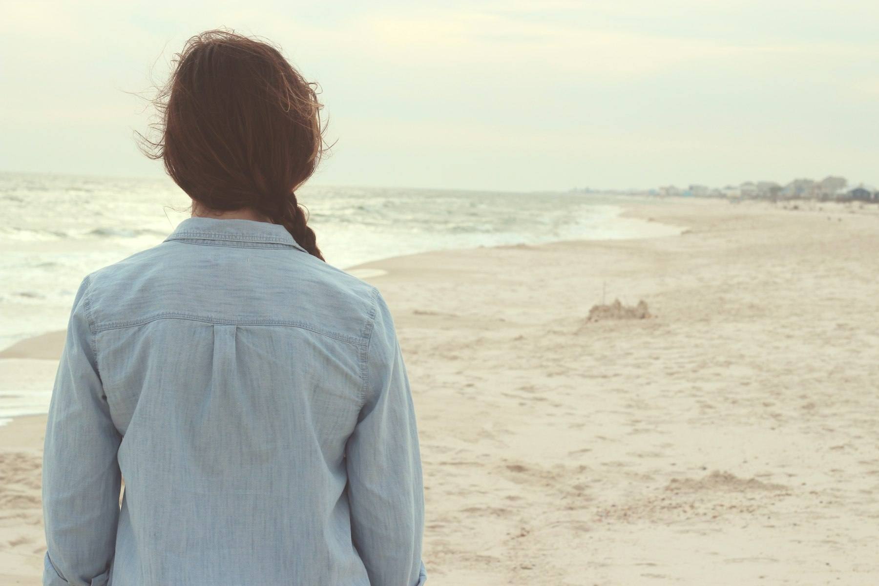 A woman standing on a sandy beach looking out across the sea
